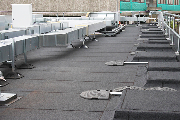 Felt roofing South East- Flat felt roofing system with rooftop plant supports and ventilation units on a commercial building.