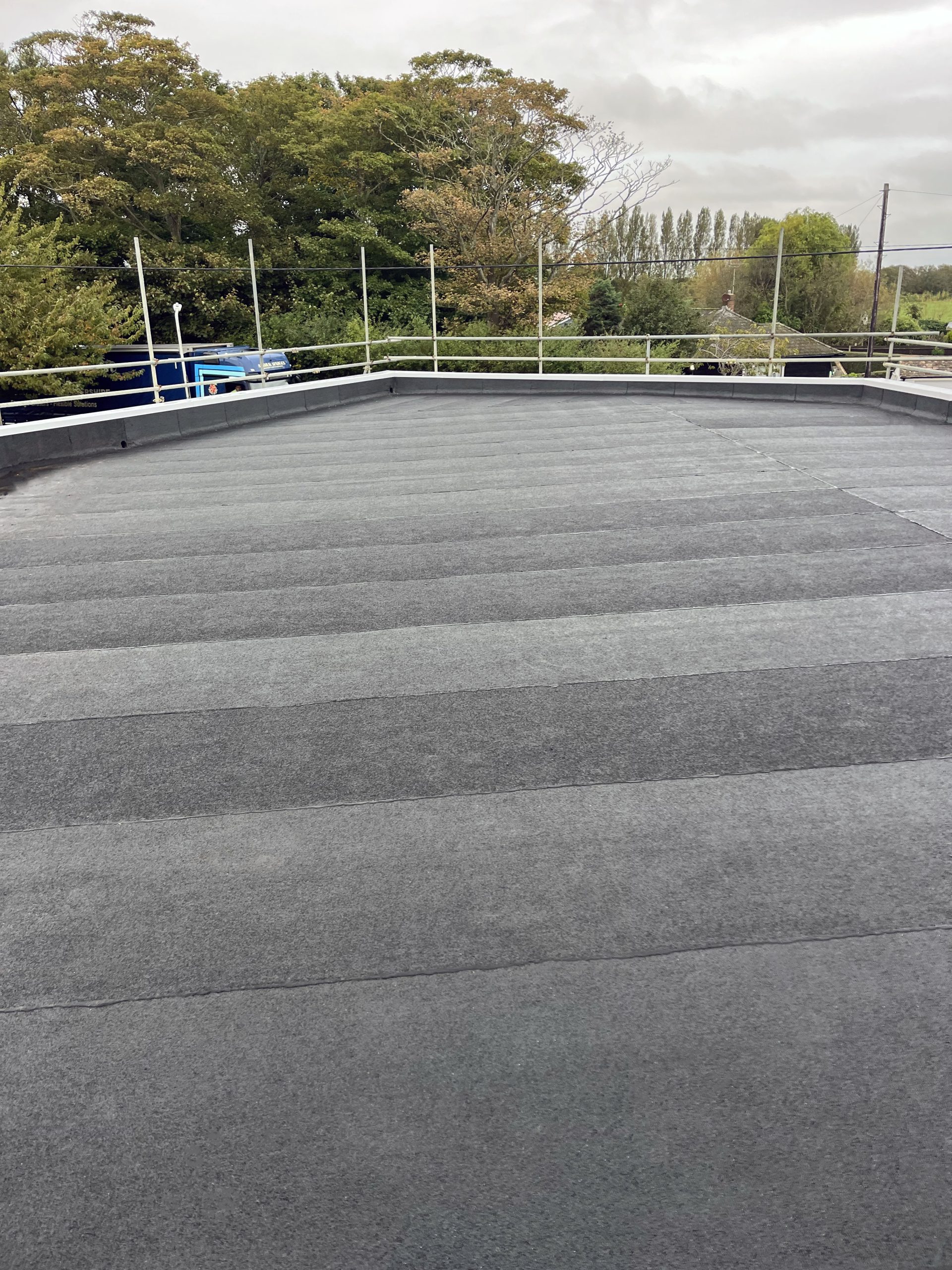 Felt roofing South East – wide flat roof surface with torch-on felt membrane and safety railings