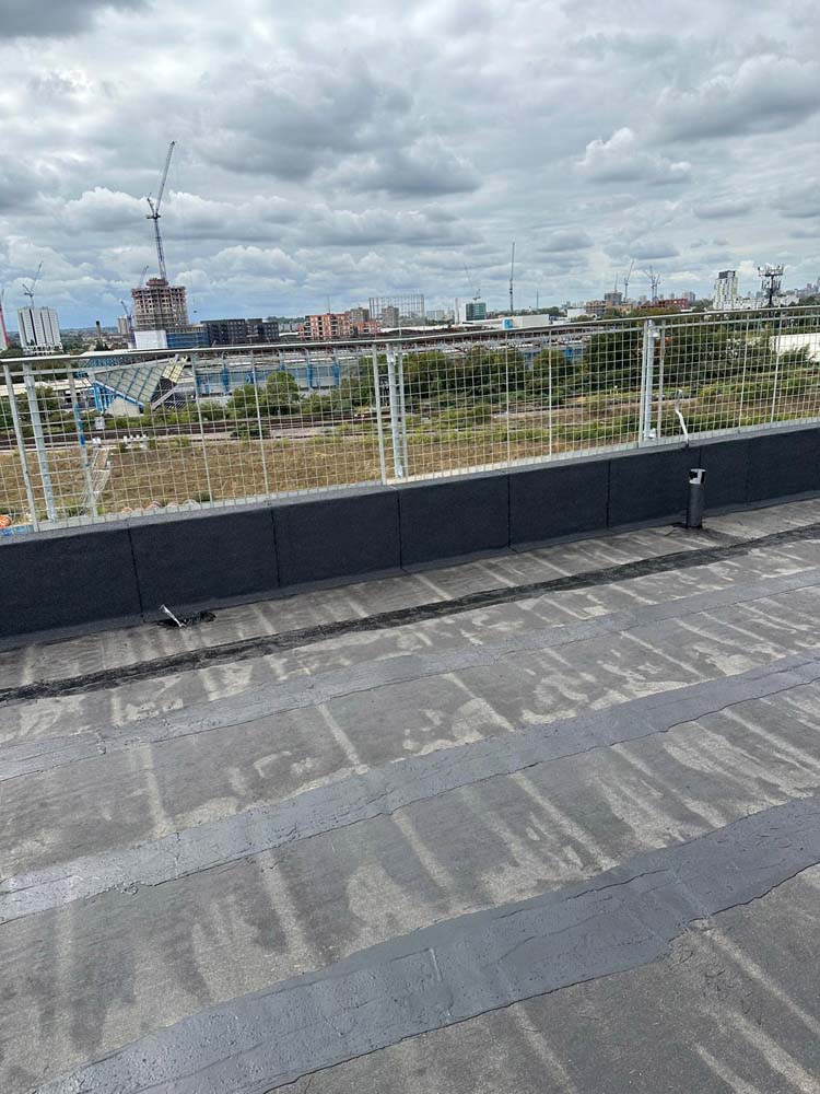 Hot Melt Roofing South East – hot melt flat roof nearing completion on commercial building with city skyline view