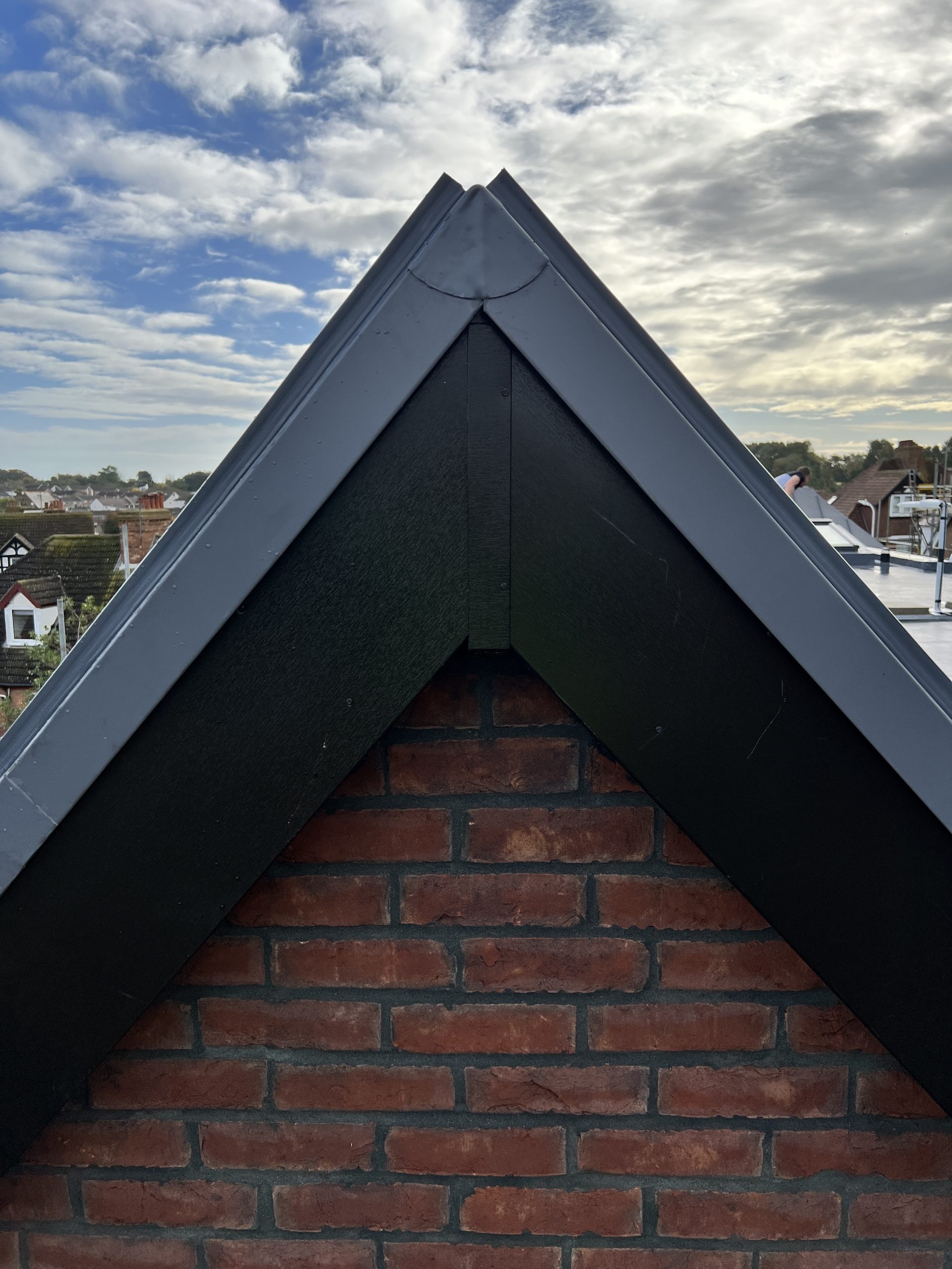 Gable-end view of single ply vertical roof installation on red brick wall under cloudy sky