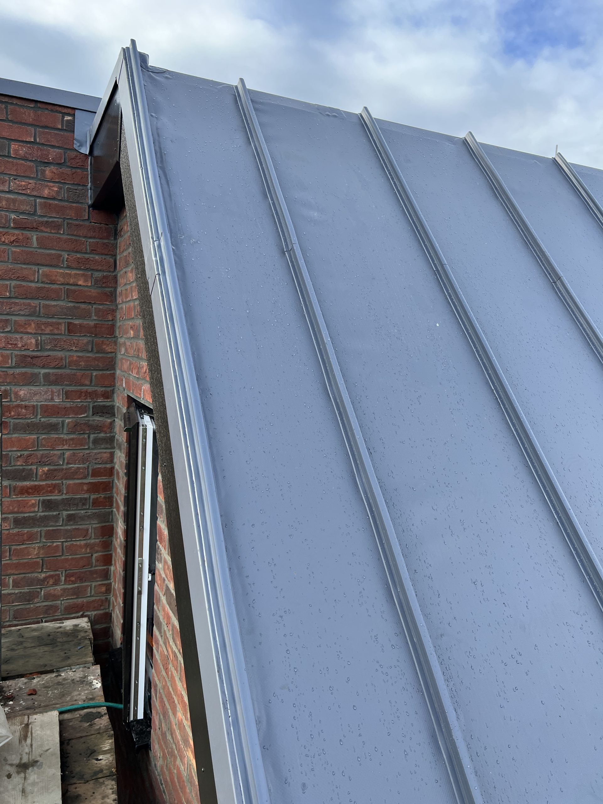 Tall vertical single ply membrane installation with standing seam appearance on brick facade