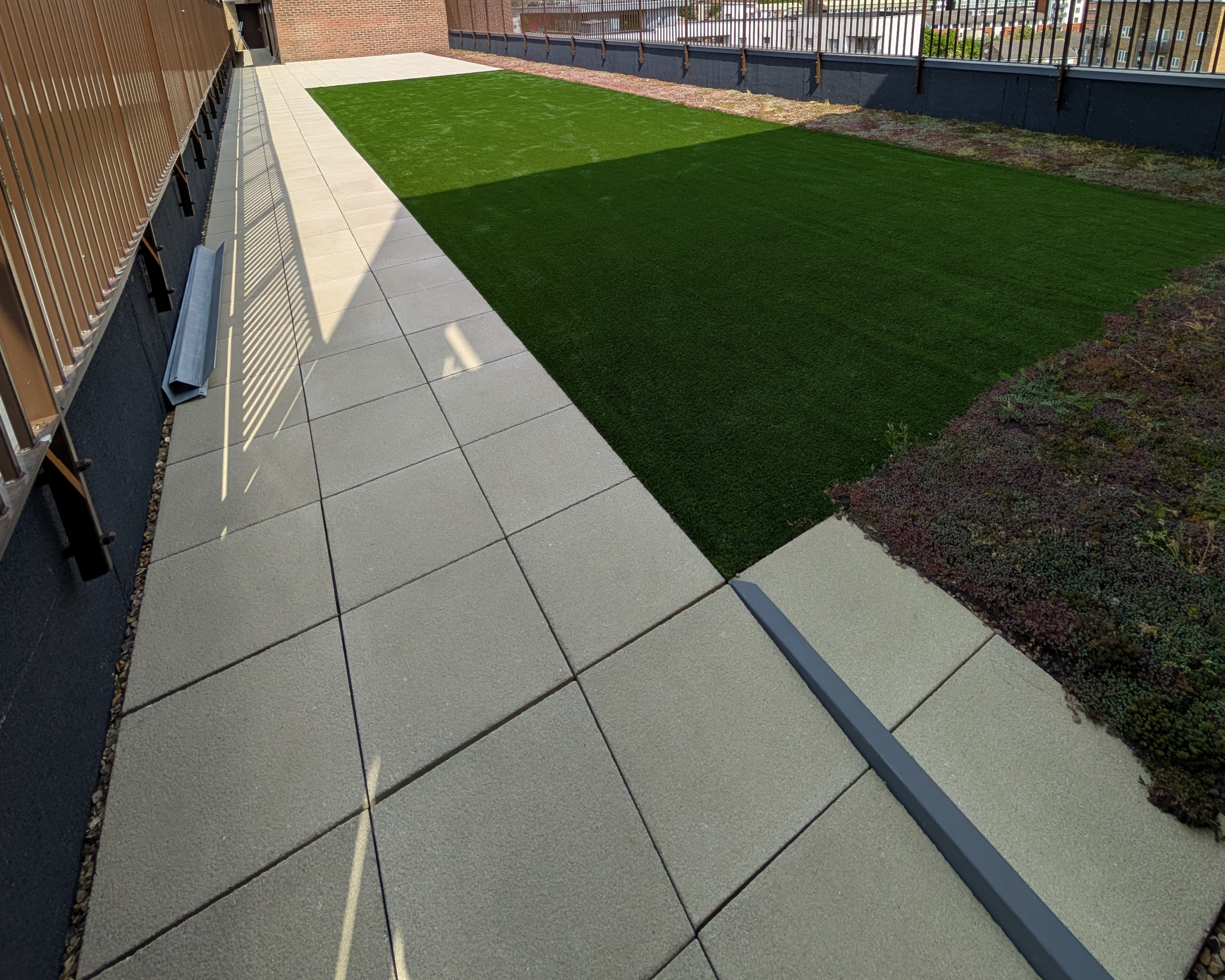 Concrete slab patio with artificial grass and a sedum roofing system on a brand-new roof terrace in London. AJ Lucas Roofing | Roofing Contractors South East & London