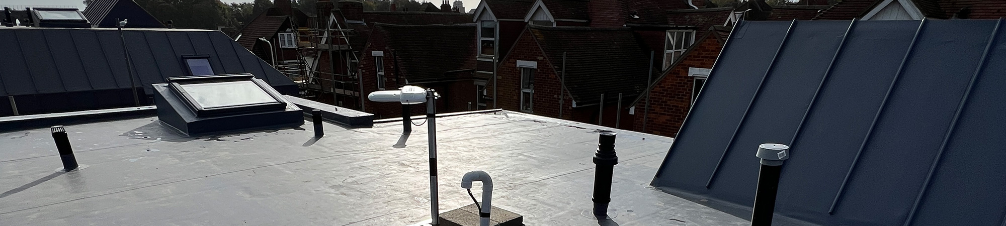 Single ply flat roofing system with pipe penetrations and skylight on a residential building under clear sky.