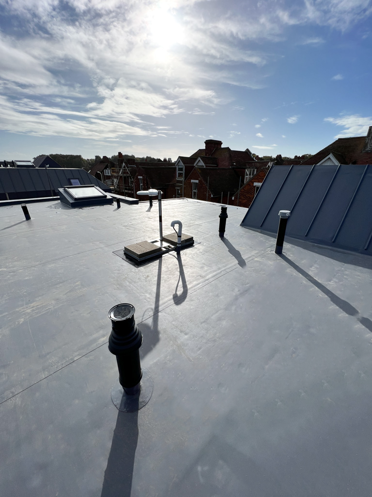 Single ply flat roofing system with pipe penetrations and skylight on a residential building under clear sky